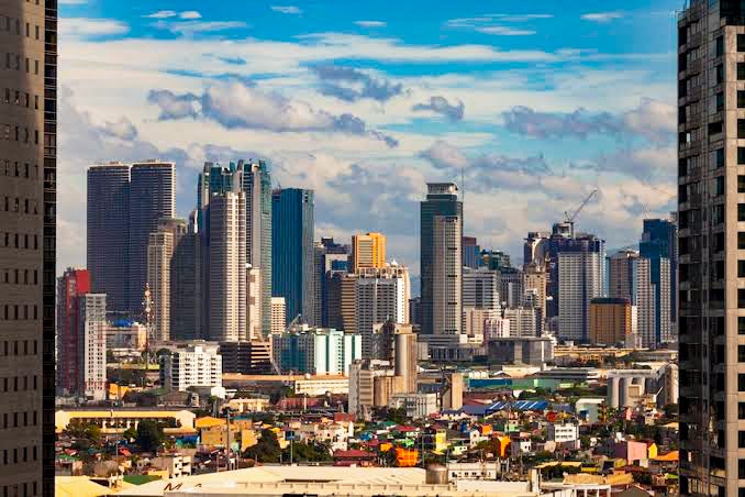 A panoramic view of the Manila skyline showcasing a mix of modern skyscrapers and residential buildings under a vibrant blue sky with scattered clouds.