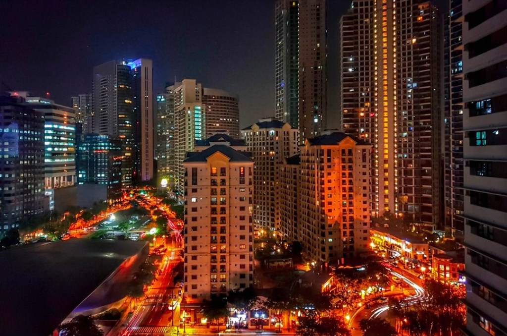 Night view of a busy urban area in the Philippines, showcasing high-rise buildings, illuminated streets, and bustling city life.