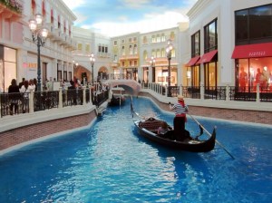 A scenic view of the Venice Grand Canal Mall in McKinley Hill, Taguig City, featuring a gondola on a blue waterway surrounded by stylish shops and restaurants.