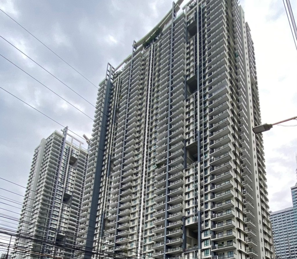 A view of two tall residential buildings showcasing modern architecture, featuring numerous balconies and a contemporary design under a cloudy sky.