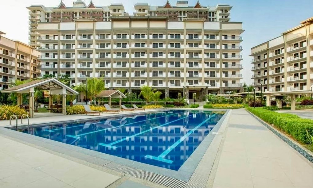 A view of a residential complex with several buildings surrounding a swimming pool and landscaped areas, showcasing modern architecture and amenities.