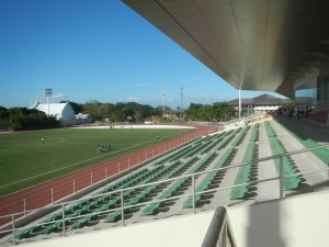 A view of a modern sports stadium in Biñan, Laguna, featuring a green football field and seating area under clear blue skies.