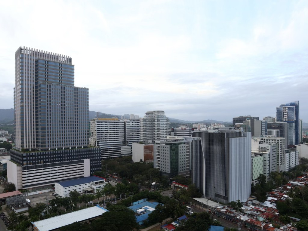 A skyline view of a modern urban area featuring tall buildings and commercial structures, showcasing a blend of architectural styles and greenery in the vicinity.
