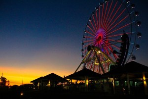 Silhouette of a ferris wheel with colorful lights against a sunset sky, showcasing a leisure destination.