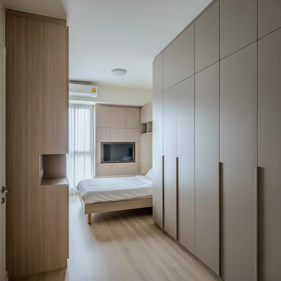 Modern bedroom interior featuring a bed, built-in cabinets, and a wall-mounted TV, with natural light coming through sheer curtains.