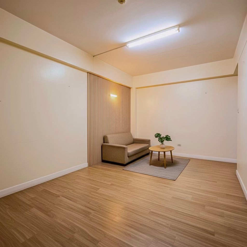 A cozy living area in a condo featuring a light-colored sofa, a round wooden coffee table, and a small plant on a circular rug, with modern paneling on the wall and sufficient overhead lighting.