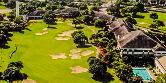 Aerial view of a lush golf course with manicured greens, sand traps, and a clubhouse in the background.