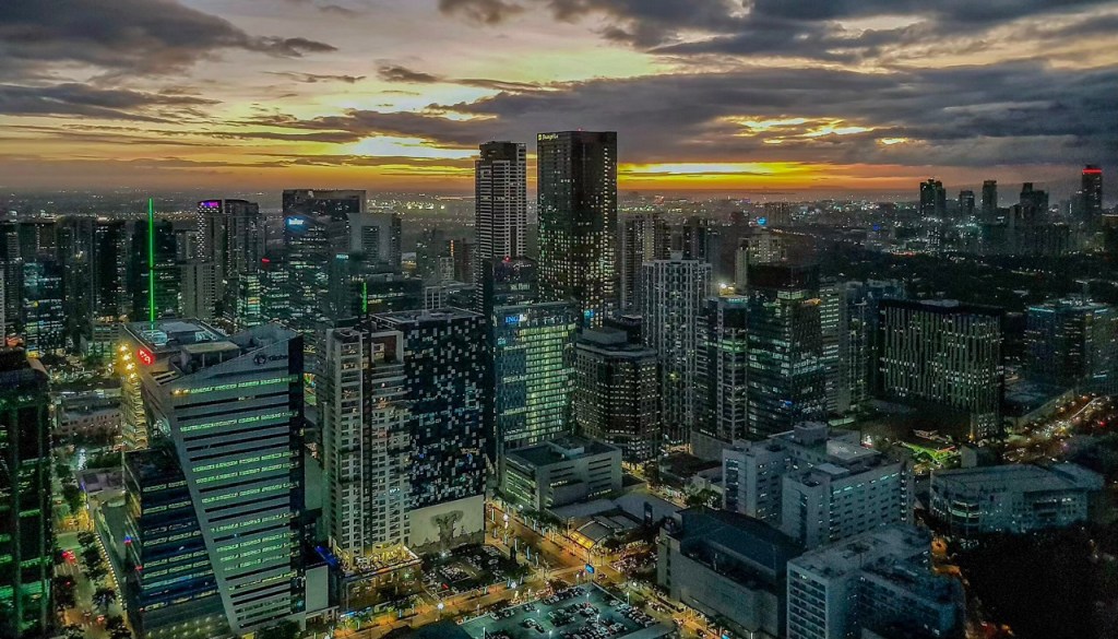 Aerial view of a vibrant cityscape at dusk, showcasing tall buildings and a sunset sky with shades of orange and purple.