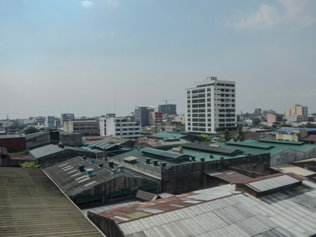A city skyline view showing a mix of modern buildings and older structures with green roofs against a clear sky.