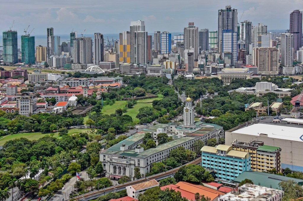 Aerial view of a vibrant urban landscape featuring modern skyscrapers and historic buildings amidst green parks, showcasing the city skyline and lush vegetation.