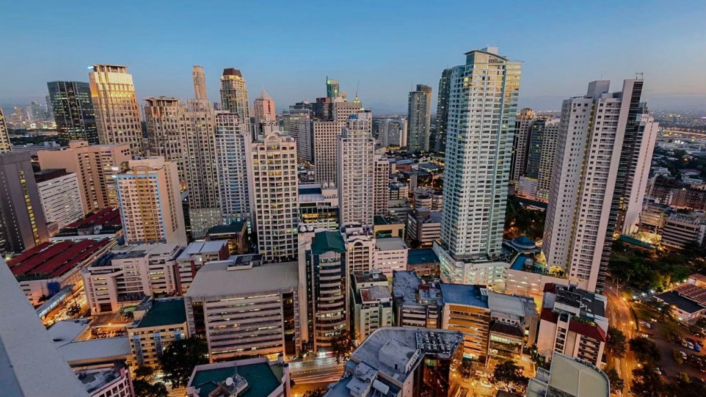 A panoramic view of a bustling city skyline during twilight, showcasing a mix of modern skyscrapers and buildings with lights beginning to illuminate the streets below.
